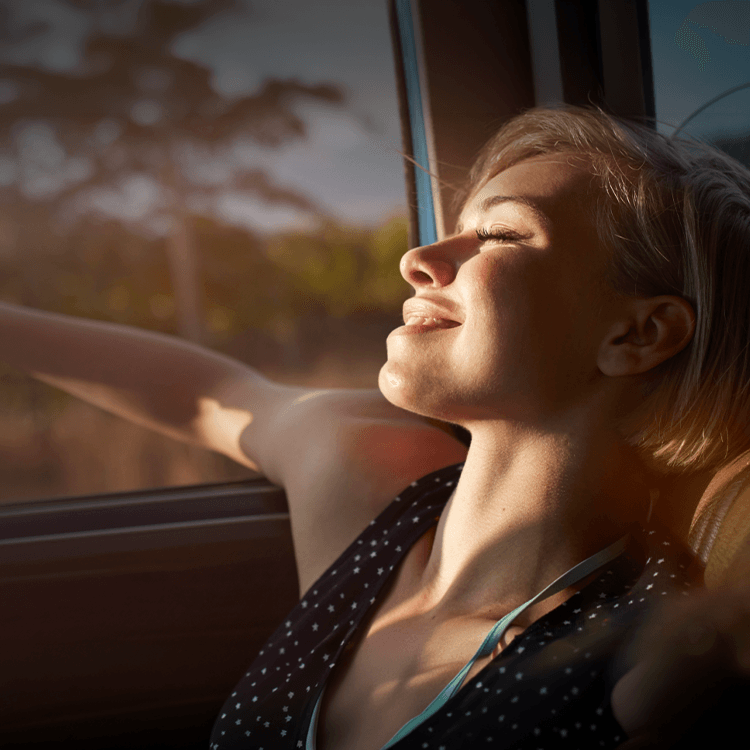 Person genießt Sonnenlicht durch Autofenster, entspannt mit geschlossenen Augen während der Fahrt im Nissan.
